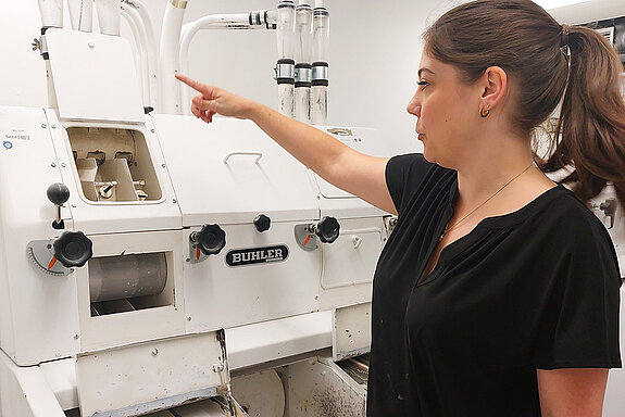 Junge Frau steht vor einer weißen Mühle und zeigt nach oben.