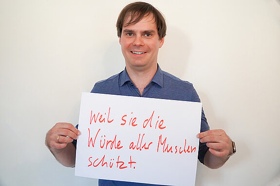 Stadtratsmitglied Dr. Andreas Mehltretter. Foto: Stadt Freising Ein Mann in einem blauen Hemd zeigt ein Schild mit der Aufschrift "weil sie die Würde der Menschen schützt"