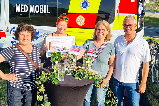 Drei Frauen und ein Mann um einen Stehtisch Im Hintergrund das gelb-rote Medmobil