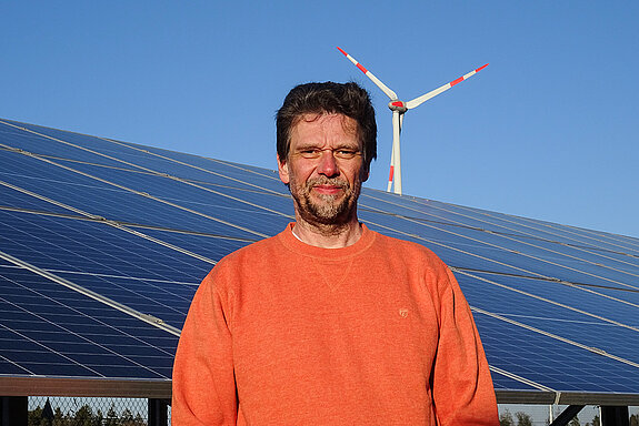 Andreas Henze im roten Shirt vor Solarmodulen und einem Windrad