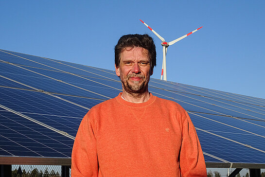 Andreas Henze im roten Shirt vor Solarmodulen und einem Windrad