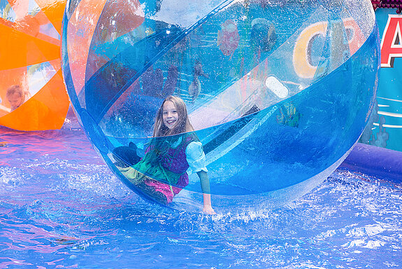 Beim "Waterball" ist man/frau im Ball und versucht, aufrecht stehen zu bleiben - den Kindern gelingt das insgesamt ganz gut. (Foto: Stadt Freising)