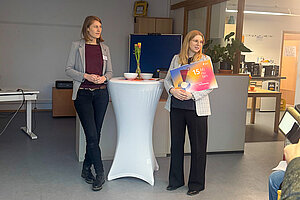 Die Geschäftführerinnen des kjr bei der Vorstellung des Kalenders. Links Birgit Irrgang, rechts Martha Klingel. Foto: kjr Freising zwei Frauen stehen neben einen Stehtisch, eine hat einen großen Kalender in der Hand