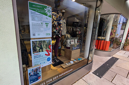 Das DAV-Fenster im Freiluftwerk warb für Engagement für Klimaschutz. Foto: Stadt Freising Neben Schaufensterpuppen in Bergbekleidung hängen 2 Plakate: "Klimaneutral bis 2030" und Menschen, die Wege instand setzen.