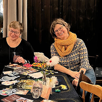 zwei Frauen an einem Tisch mit vielfältigen Materialien