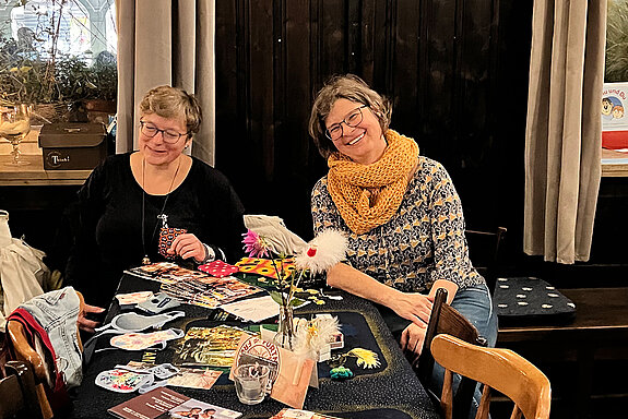 zwei Frauen an einem Tisch mit vielfältigen Materialien