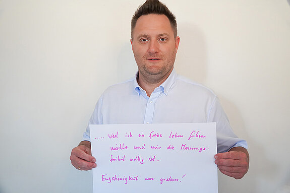 Stadtratsmitglied Robert Weller. Foto: Stadt Freising Ein Mann in einem weißen Hemd zeigt ein Schild mit der Aufschrift "weil ich ein freies Leben führen möchte und mir die Meinungsfreiheit wichtig ist. Engstirnigkeit war gestern!"