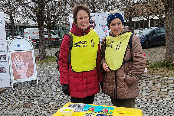 Amnesty suchte Unterstützung für die Menschenrechtskampagnen. Foto: Amnesty Freising zwei Frauen mit Amnesty-Warnwesten hinter einem Infotisch