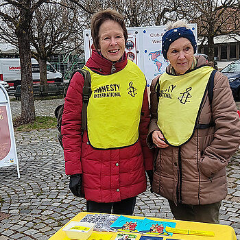 Amnesty suchte Unterstützung für die Menschenrechtskampagnen. Foto: Amnesty Freising zwei Frauen mit Amnesty-Warnwesten hinter einem Infotisch