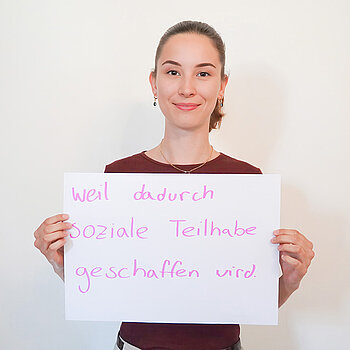 Stadtratsmitglied Rosalie Freitag. Foto: Stadt Freising Eine Frau in einem roten T-Shirt zeigt ein Schild mit der Aufschrift "weil dadurch soziale Teilnahme geschaffen wird."