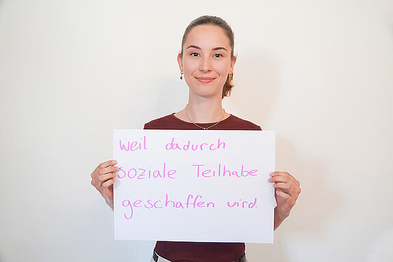 Stadtratsmitglied Rosalie Freitag. Foto: Stadt Freising Eine Frau in einem roten T-Shirt zeigt ein Schild mit der Aufschrift "weil dadurch soziale Teilnahme geschaffen wird."