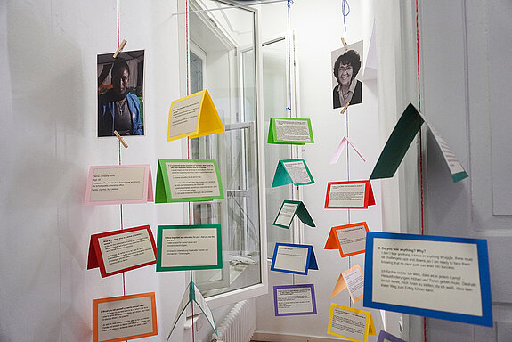 Bunte Karten mit Text beschrieben und Fotos an Schnüren aufgehängt.
