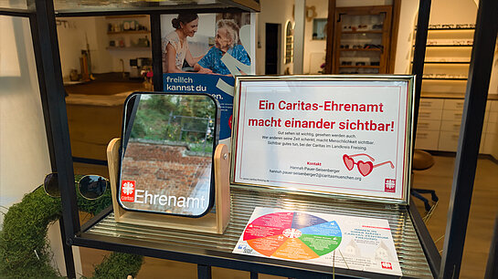"Ein Caritas-Ehrenamt macht einander sichtbar" bei Optiker Sichtbar. Foto: Stadt Freising Ein Spiegel mit "Caritas Ehrenamt" Aufdruck und ein Text im Bilderrahmen. "Gut sehen ist wichtig, gesehen werden auch."