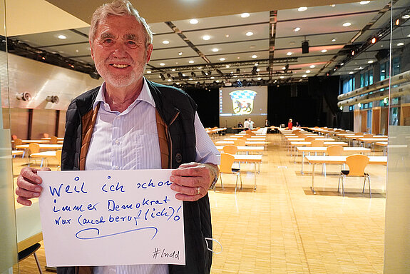 Stadtrat Hartmut Binner hält ein Schild mit der Aufschrift: "weil ich schon immer Demokrat war (auch beruflich)!"