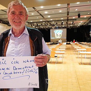 Stadtrat Hartmut Binner hält ein Schild mit der Aufschrift: "weil ich schon immer Demokrat war (auch beruflich)!"