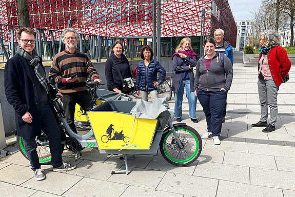 Eine Gruppe Menschen steht um ein gelbes Lastenrad mit Bärenlogo darauf.