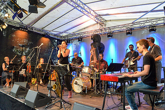 Julia Schröter (Gesang) mit (von rechts) Lukas F. Voith (Keybord) , Häns Czernik (Gitarre), Yvo Fischer (Bass), Stephan Treutter (Schlagzeug), Vipo Maat (Gitarre) und der Streicherbegleitung. (Foto: Stadt Freising)