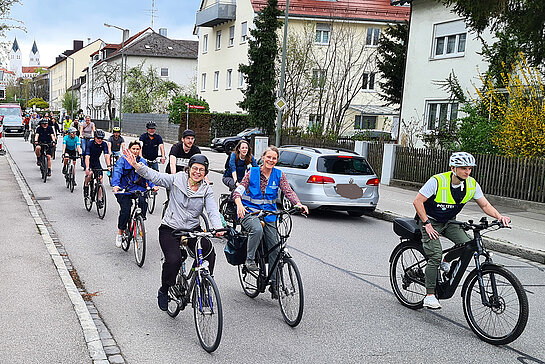 Eine Gruppe von 10-20 Radfahrern fährt teilweise winkend durch einen Straße. Im Hintergrund die Domtürme