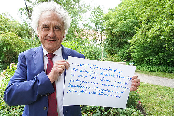 Landrat Helmut Petz hält ein Schild mit der Aufschrift: "weil Demokratie die einzige Staatsform ist, in der ich leben möchte, getragen von verantwortungsbewussten Menschen mit Sinn für das Gemeinwohl!"