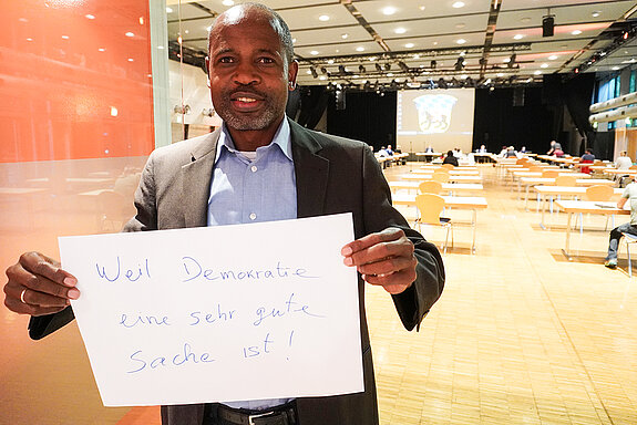 Migrationsreferent Samuel Fosso ält ein Schild mit der Aufschrift: "weil Demokrate eine sehr gute Sache ist."