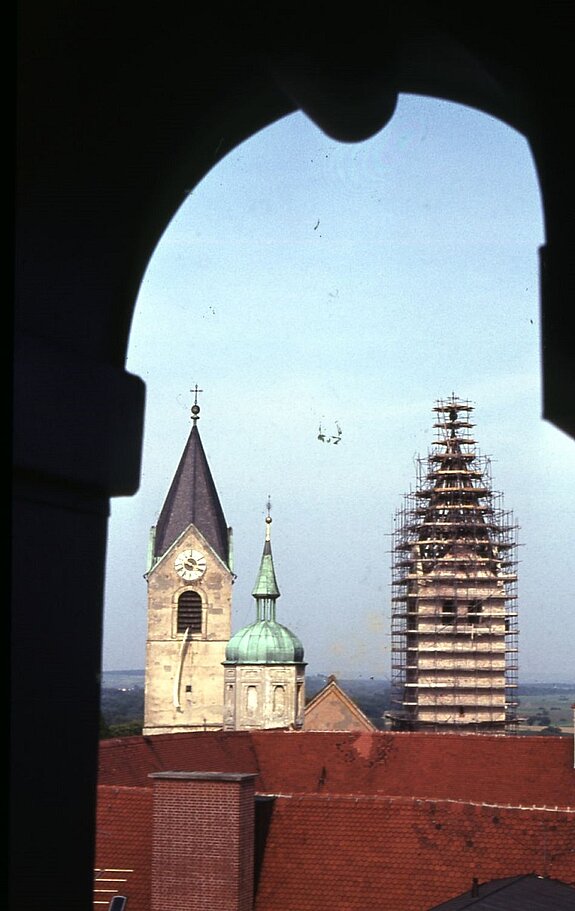 Die Domtürme von Westen, 1962. Die Neugestaltung des Südturms ist gerade in vollem Gange, der Nordturm ist noch unverändert. Zwischen den Domtürmen spitzt der 1965 abge-brochene Westgiebel hervor, im Vordergrund ist der kleine Residenzturm zu sehen. Fotograf Alois Lutzenberger steht in der Kuppellaterne des Süderkers des Klerikal-Seminars (sog. „Seidl-Turm“, 2022 abgebrochen).