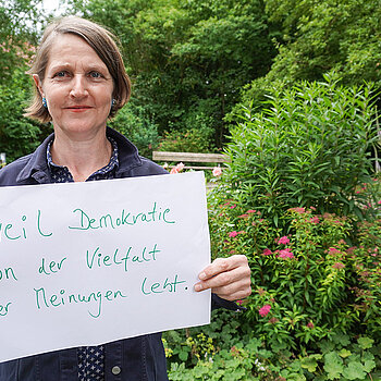 Susanne Höck, engagiert im Fairen Forum hält ein Schild mit der Aufschrift: "weil Demokratie von der Vielfalt der Meinungen lebt."