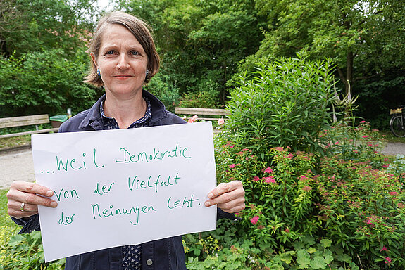 Susanne Höck, engagiert im Fairen Forum hält ein Schild mit der Aufschrift: "weil Demokratie von der Vielfalt der Meinungen lebt."