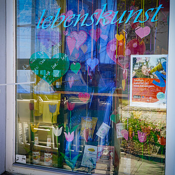 Tulpen, Herzen und ein Plakat im Fenster, darüber in blau "Lebenskunst"