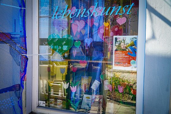 Tulpen, Herzen und ein Plakat im Fenster, darüber in blau "Lebenskunst"