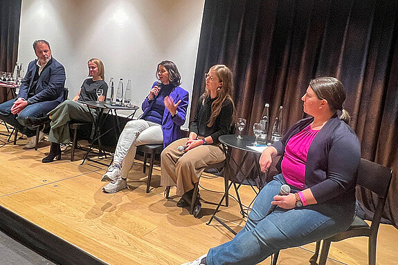4 Frauen und ein Mann sitzen auf einem Podium auf Stühlen