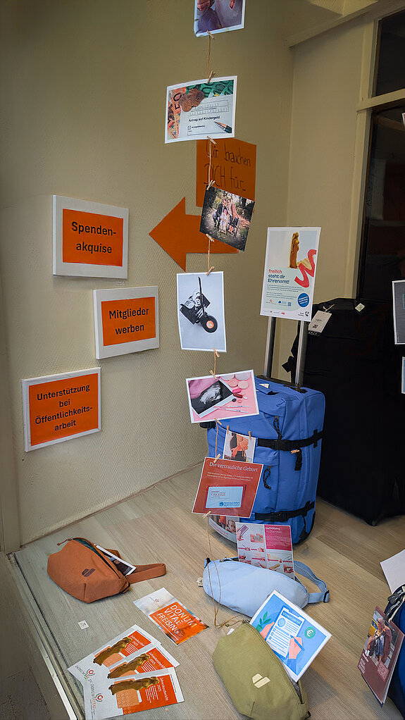Donum Vitae suchte im Fenster von Birnkammer Unterstützung. Foto: Stadt Freising Neben Rücksäcken und Taschen sind orange Schilder an der Seitenwand, Karten hängen mit Wäscheklammern an einer Schnur.
