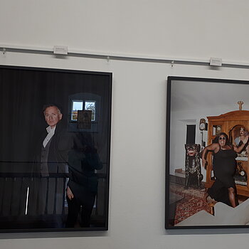Zwei großformatige Fotos, ein Mann vor schwarzem Vorhang und eine junge Frau, die durch ein Zimmer hüpft.
