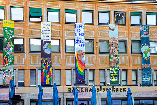 Zu sehen sind bunt bemalte Banner an einer Hausfassade am Marienplatz. Diese haben Kinder mit Texten zum Thema Demokratie, Frieden und Liebe gestaltet. (Foto: Stadt Freising) 