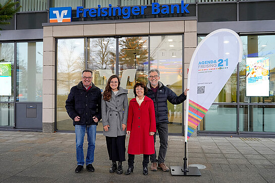 von links nach rechts: Rainer Teschner, Referent; Sandra Neumayer, Freisinger Bank; Marita Hanold und Sepp Beck, Sprecher der Agenda. Foto: Freisinger Bankund... zwei Männer und zwei Frauen stehen in Winterkleidung von der Freisinger Bank und haben eine Agenda-Beachflag dabei