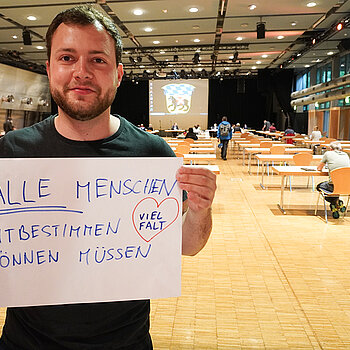 Jugendreferent Nico Heitz hält ein Schild mit der Aufschrift: "alle Menschen mitbestimmen können müssen. Vielfalt"