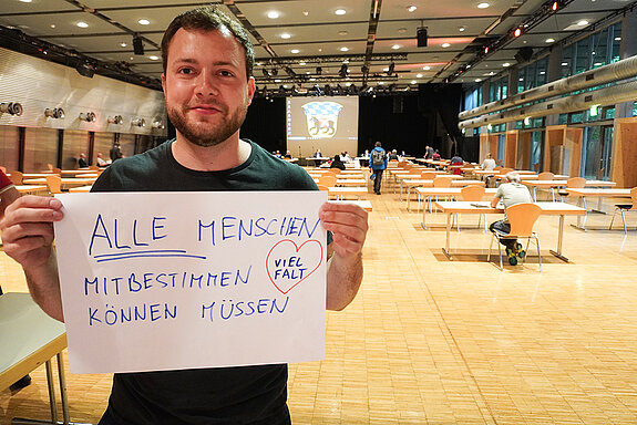 Jugendreferent Nico Heitz hält ein Schild mit der Aufschrift: "alle Menschen mitbestimmen können müssen. Vielfalt"