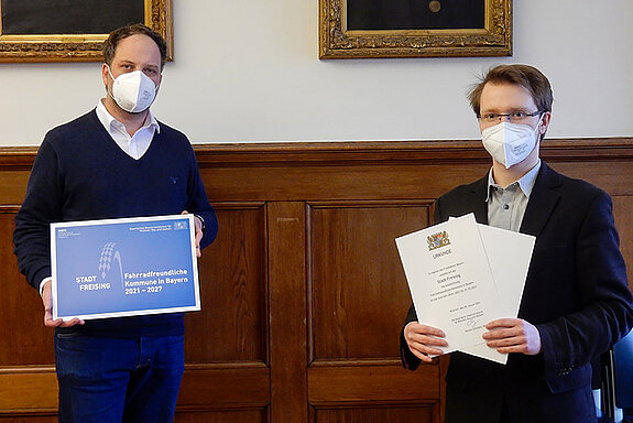 Freising ist als fahrradfreundliche Kommune zertifiziert: Mobilitätsbeauftragter Dominik Fuchs (rechts) übergibt die Urkunde und die mit der Auszeichnung verbundene Tafel an OB Tobias Eschenbacher. (Foto: Stadt Freising)