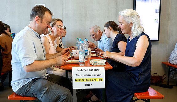 Für diese Gruppe gabs nur Reis - aber immerhin wurden die Teilnehmenden satt. Foto: Marco Einfeldt An einem Tisch sitzen sich Teilnehmer und Teilnehmerinnnen gegenüber, die nur Reis zum Dinner bekommen.