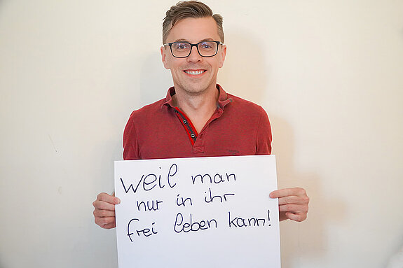 Stadtratsmitglied Dr. Jens Barschdorf. Foto: Stadt Freising Ein Mann in einem roten Hemd zeigt ein Schild mit der Aufschrift: "weil man nur in ihr frei leben kann!"